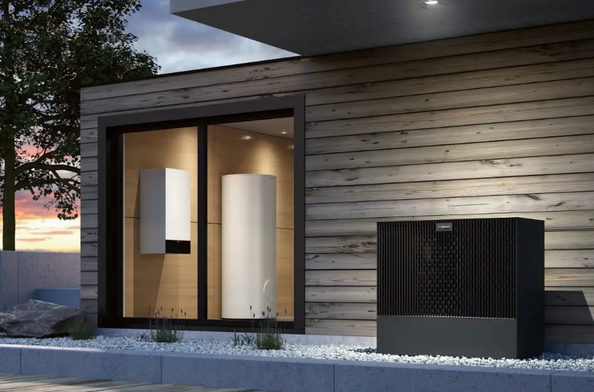 Moderne Luft-Wasser-W&auml;rmepumpe vor einem deutschen Einfamilienhaus, im Hintergrund ein klassischer Gasz&auml;hler &ndash; visueller Vergleich zweier Heiztechnologien f&uuml;r die Heizungsmodernisierung 2026